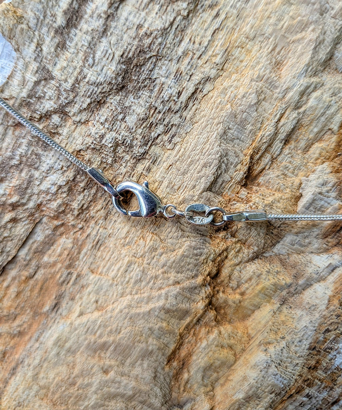 Close-up of a silver chain necklace with a lobster clasp, laid on a textured wood surface.